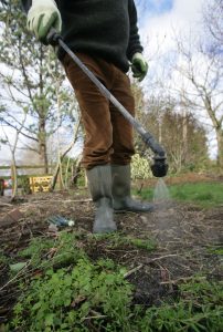 Gardener stands with boots and gloves with a hose.